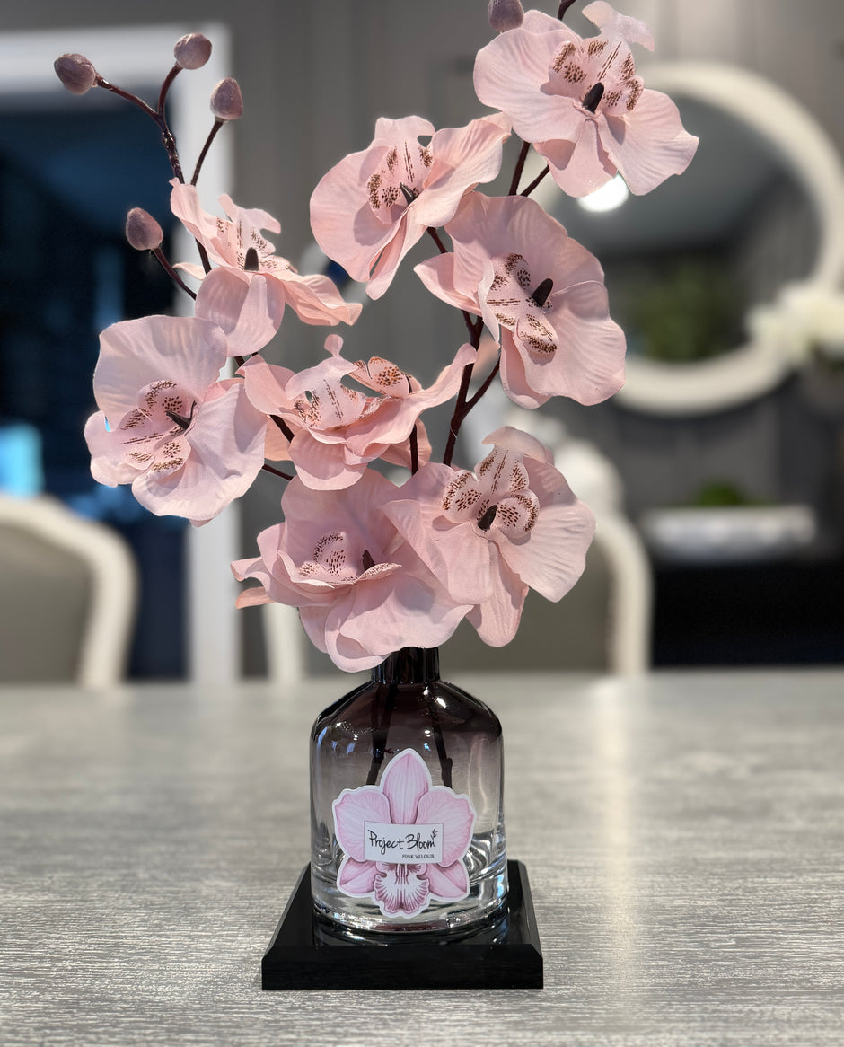 Pink orchid arrangement in a glass vase on a table with a blurred background